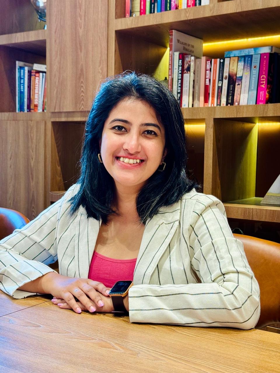 Neha Nagwekar, founder of Branding Brews, smiling at a table in front of a bookshelf